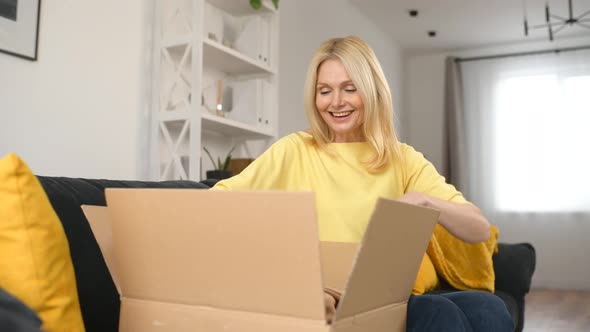 Stylish Middleaged Blonde Woman Sitting on the Couch with Carton Box on Laps