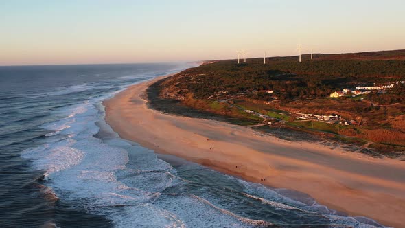 Praia do Norte Beach in Nazare Portugal with string waves and wind turbines in the distance, Aerial