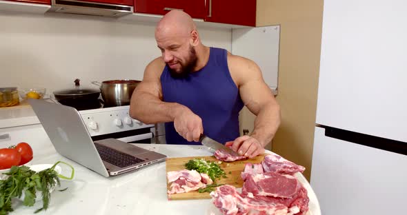 Bald Man Is Browsing Internet Site By Notebook and Cutting Meat in Kitchen