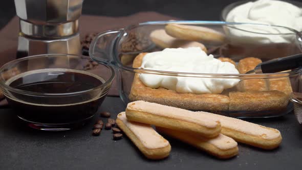 Italian Savoiardi Ladyfingers Biscuits and Cream in Baking Dish, Coffe Maker on Concrete Background