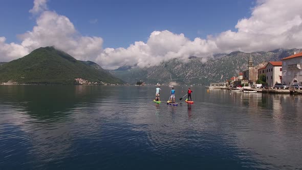 Surfers Float on Surfboards Past Perast