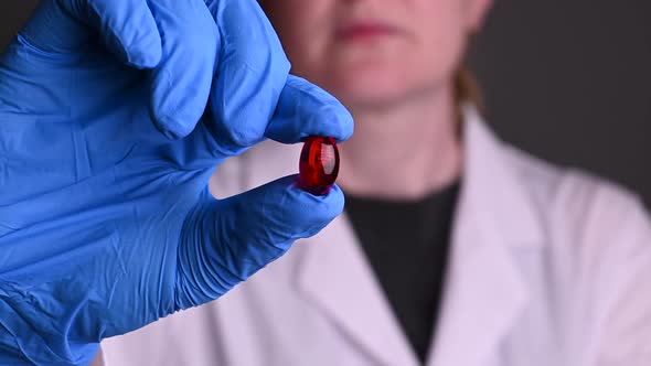 Red Pill in Hand. Gloves and a White Robe. Treatment of Diseases and Viruses. Epidemic Covid