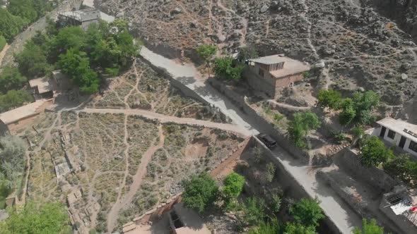 Aerial View Of Car Travelling Through Road In Village Hillside In Kalash Valley In Pakistan. Follow