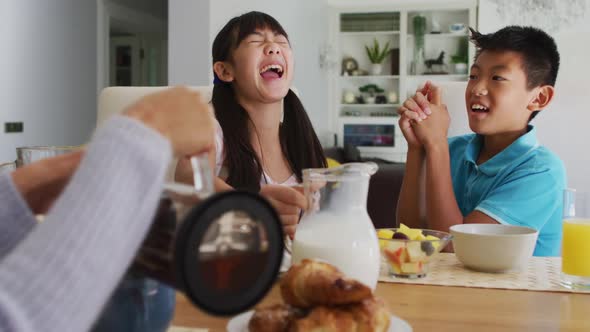 Happy asian brother and sister in kitchen having breakfast and laughing with parents