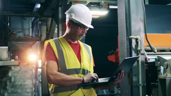 Engineering Expert with a Laptop is Watching Factory Machinery