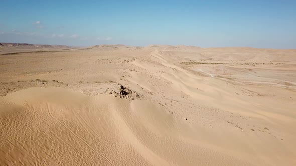 Aerial shot in low attitude of dry desert. Desert landscape with dunes and mountains. Empty golden b