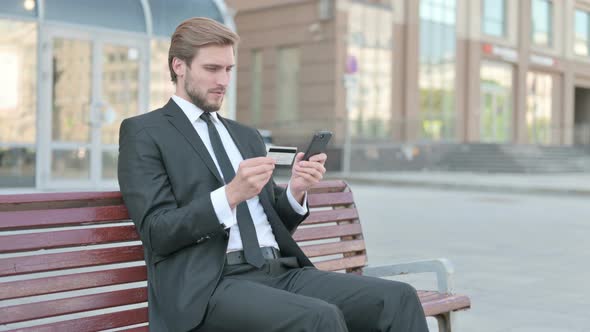 Excited Businessman Shopping Online Via Smartphone Sitting Outdoor
