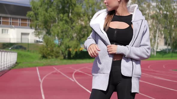 Slim Athletic Woman Putting on Earphones While Standing on Athletic Field