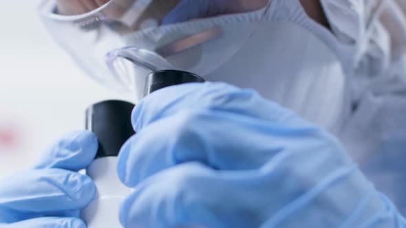 Close Up Low Angle Shot of Scientist in Mask and Protective Glasses Looking Into the Microscope