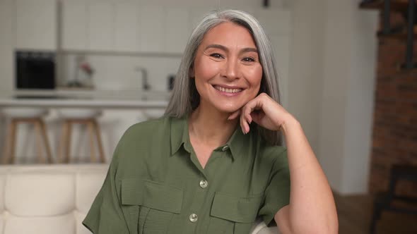 Portrait of Attractive Middleaged Woman with Long Silver Hair Sitting in Modern Apartment