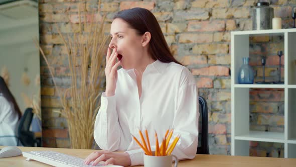 Tired Young Businesswoman Using Computer and Yawning in Office