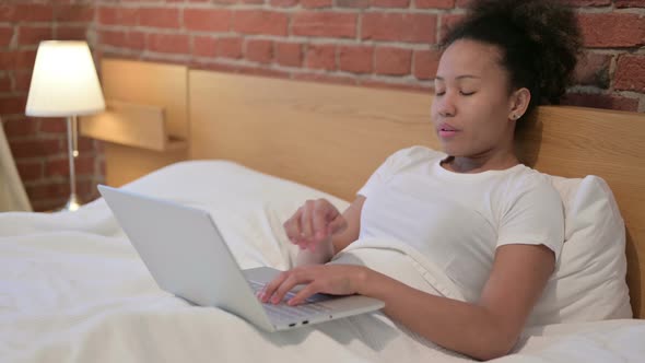 Young African Woman Thinking and Working on Laptop in Bed