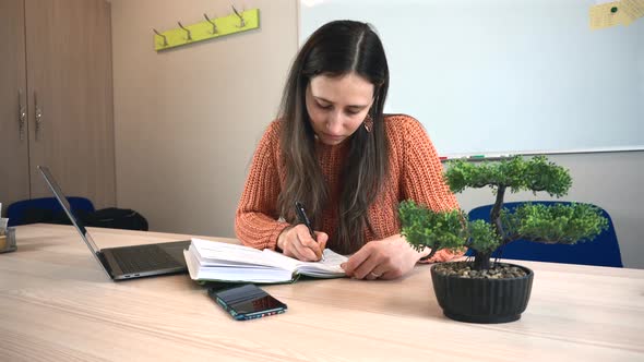 Footage of young woman sitting in office and making notes in planner, manage your time.