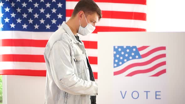 American Man in a Denim Jacket and a Mask Votes in a Voting Booth. US Elections 2020 During the