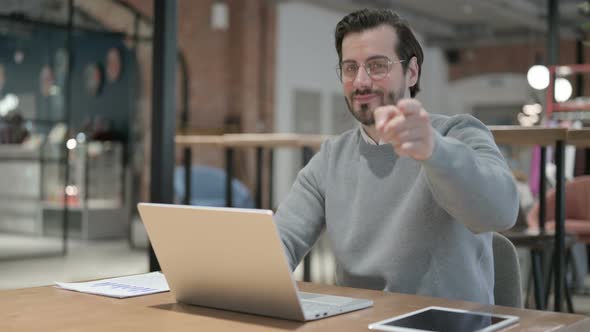 Young Man Pointing at Camera While Using Laptop in Office