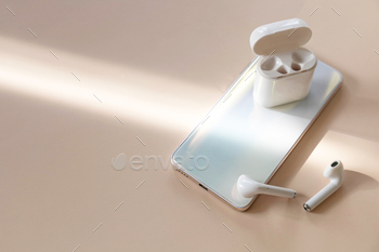 one smartphone and of a pair of white wireless headphones on a pastel neutral colors background. Copy space.
