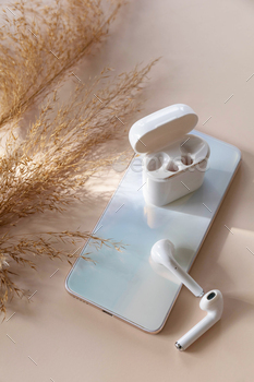 one smartphone and of a pair of white wireless headphones, dried grass on a pastel neutral colors background.