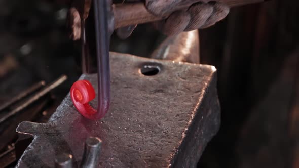 Blacksmith Bends in a Spiral an Oblong Red Heated Metal Detail By Hitting in with a Hammer