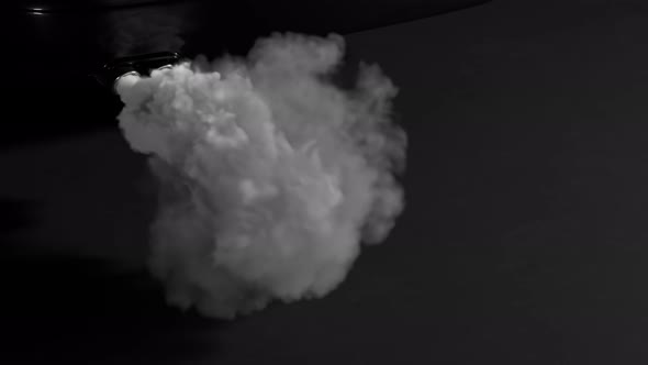 Fumes emmited from car exhaust dual pipe. White dense smoke on black background.