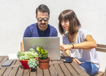  some friends with the computer, on the terrace of their home with a white background sitting at a table. Pointing to an action in the video call