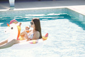 Portrait of a young girl in a swimwear on a unicorn swim ring in the pool - PhotoDune Item for Sale