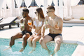 Three friends in a swimwears relaxing with a cocktails near swimming pool - PhotoDune Item for Sale