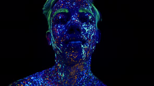 Man Covered with Phosphor Paint Looks Into Camera and Smiles in Studio on Dark Background Front View