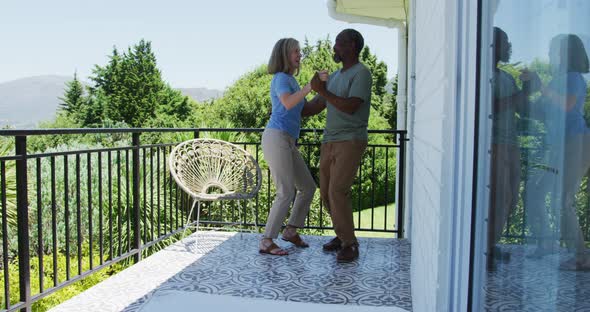 Mixed race senior couple dancing together in the balcony at home