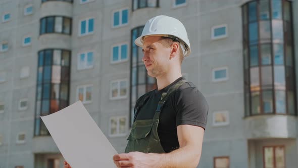 A Man in a Helmet Is Holding a Construction Plan in His Hands. A Builder Is Checking Blueprints.