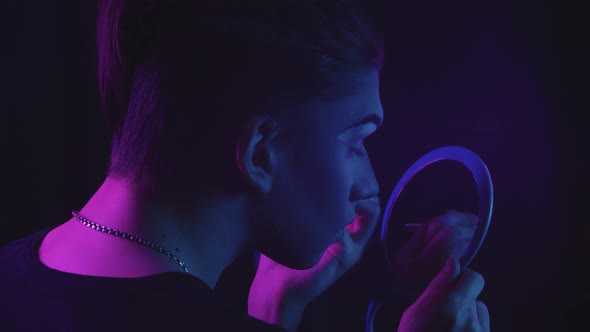 Drag Artist Young Man Drawing New Eyebrows and Looking at Himself in the Mirror Blue and Purple Neon