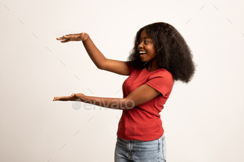 In Her Hands, Cheerful Young African American Woman Demonstrating New Item While Posing Over White Studio Background, Mockup, Copy Space