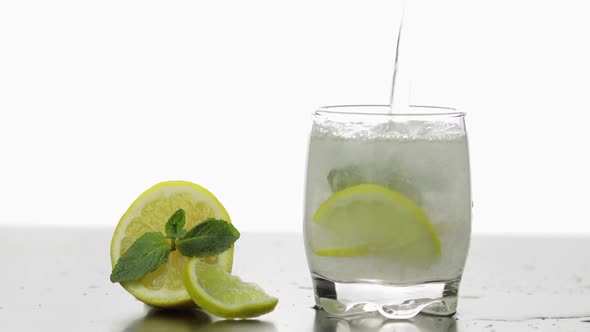 In a Glass Pour a Cold Drink with Leaves of Mint, Lime, Lemon and Ice Cubes