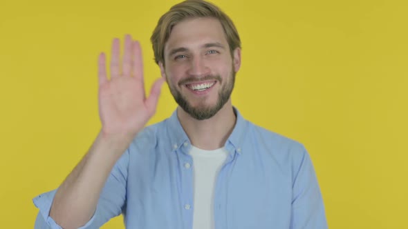 Young Man Waving Hand to Say Hello on Yellow Background