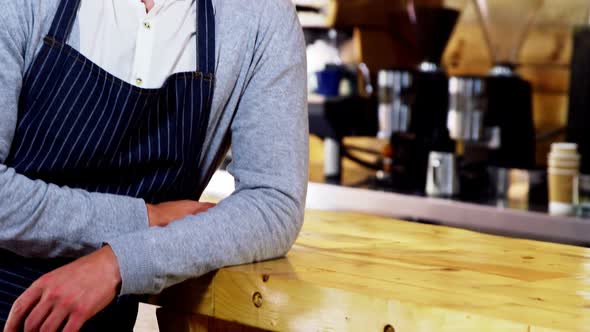 Portrait of smiling waiter leaning at counter