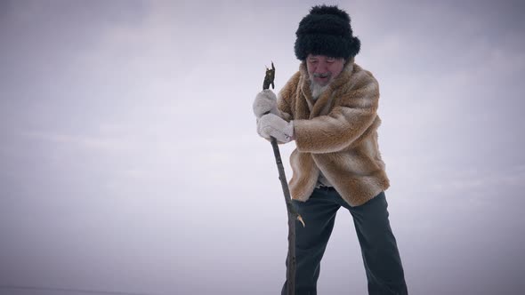 Confident Indigenous Senior Man Checking Ice with Stick Outdoors on Cold Winter Day