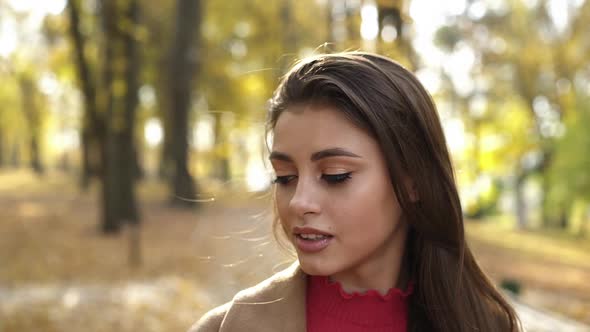 Attractive Brunette Poses with Her Long Hair and Looks at Camera in Autumn Park