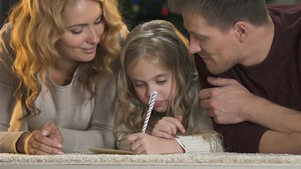 Parents Helping Daughter Write Letter to Santa Claus, Smiling Into Camera, X-Mas