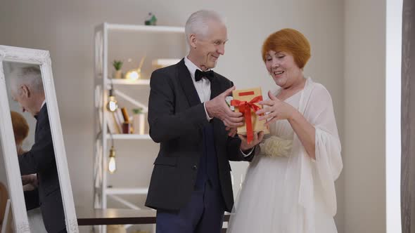 Loving Handsome Senior Groom Giving Gift Box to Excited Bride in Slow Motion