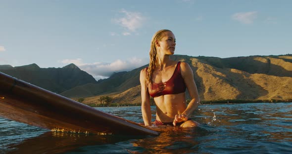 Young woman sitting on a surfboard at sunset alt