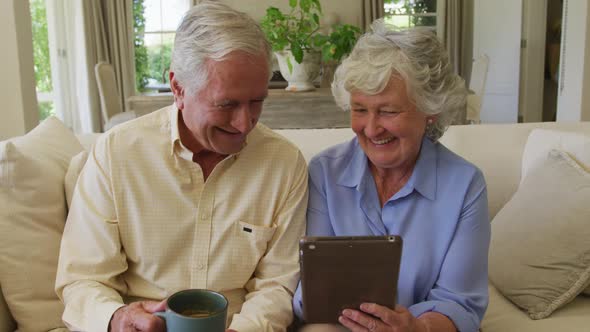 Caucasian senior couple smiling while using digital tablet together sitting on the couch at home