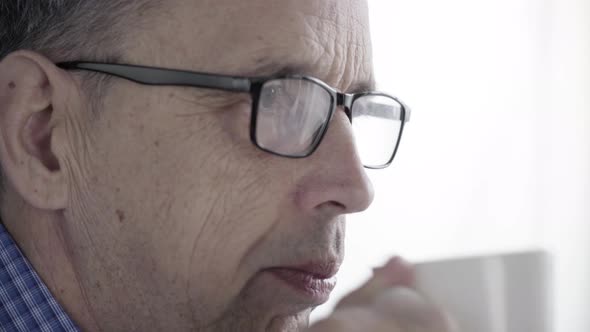 Elderly Man With Glasses Drinks Coffee or Tea From a Porcelain Mug