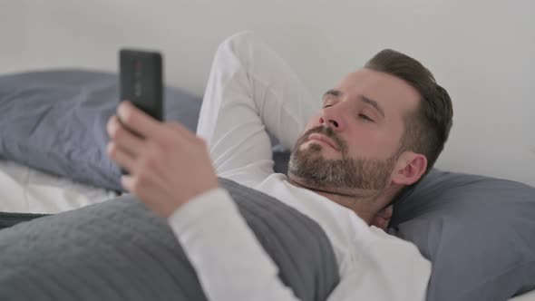 Man Using Smartphone While Laying in Bed