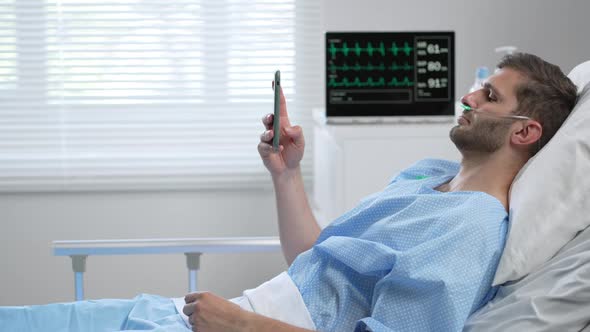 Man in Hospital with the Mobile Phone and Earphones Lying Alone in Bed
