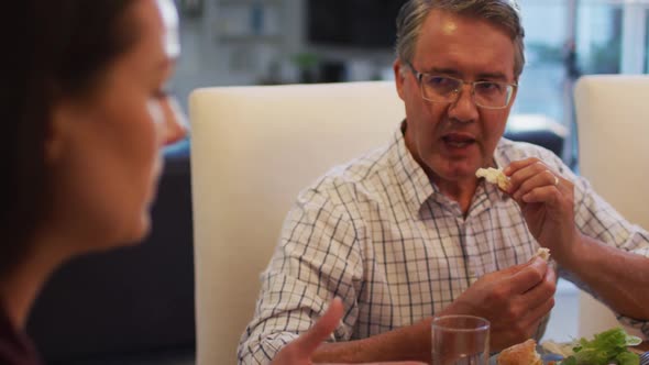 Smiling caucasian grandfather talking to daughter in law and eating at table during family meal