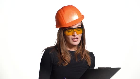 An entertaining woman in orange glasses and hard hat is holding a folder and pen