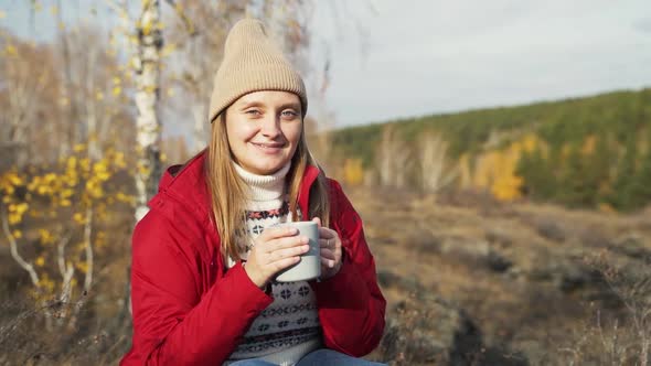 Caucasian Woman is Sitting Alone in Autumn Forest Tasting the Aroma of Tea From Gray Mug and