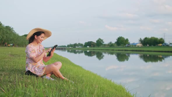 Adult woman sitting on the lawn using portable technology. Portable device tech usage concept.