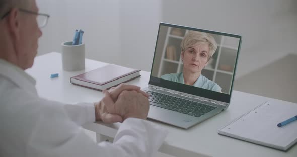 Elderly Woman Is Communicating with Doctor By Web Camera, Her Face on Laptop of Physician