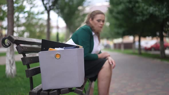 Closeup Box on Bench with Blurred Overweight Sad Caucasian Woman Sitting at Background Standing Up