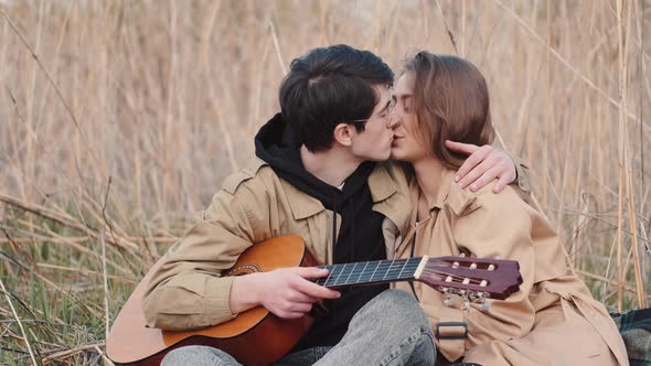 Boy with Wooden Guitar and Girl Kissing on Date in Field